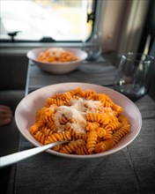 Cooked fusilli with tomato sauce and parmesan cheese on the table in the campervan
