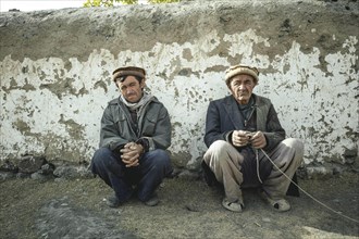 Two men squatting in front of a clay wall