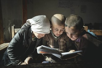 A girl and two boys reading a primer on a school desk