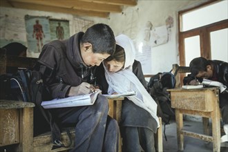A boy and a girl writing in an exercise book on a school desk