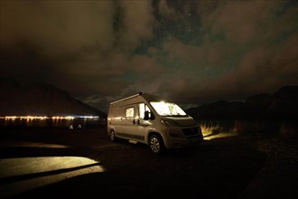 Campervan parked on parking lot near Melfjordbotn under a cloudy northern lights sky