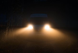 Campervan with bright lights standing in the fog