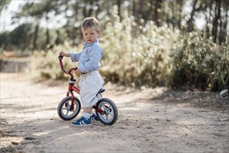Cute toddler riding his balance bicycle on a dirt road