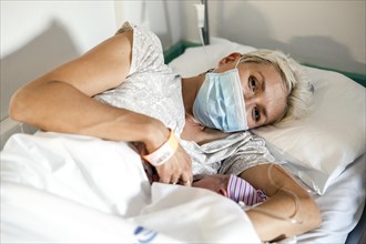 Mother wearing a respirator breastfeeds her newborn baby in hospital