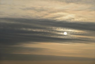 Sun shines behind layered clouds