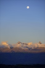 Mountain peak of the Andes above a cloud bank with full moon