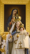 Statue of the Virgin Mary with infant Jesus and painting behind