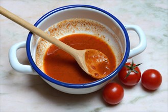Tomato soup in a bowl with cooking spoon and tomatoes