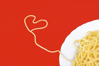 Spaghetti in heart shape on red background