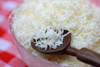Grated Parmesan cheese in glass bowl with wooden spoon