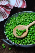 Defrosted green peas in shell with cooking spoon