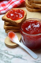 Strawberry jam in glass with spoon and rusk