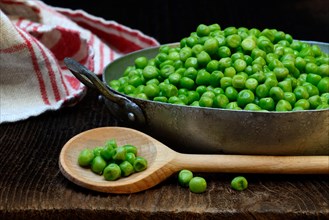 Defrosted green peas in shell with cooking spoon