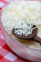 Grated Parmesan cheese in glass bowl with wooden spoon