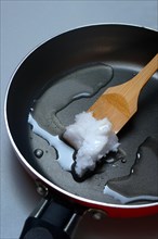 Coconut oil with bamboo spatula in frying pan
