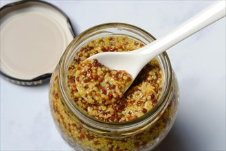 Coarse-grained mustard in glass with spoon