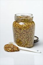 Coarse-grained mustard in glass with spoon