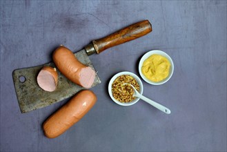Various mustard in bowls and meat sausage on cleaver