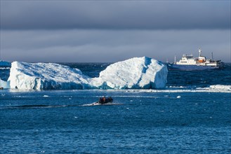 Zodiac cruising back to a cruise ship anchoring behind an iceberg
