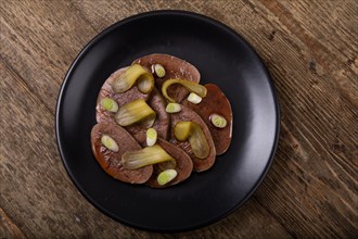 Sliced beef tongue with cornichons on black plate