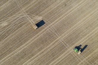 Tractor collecting bales of straw and abstract patterns in cornfield after wheat harvest
