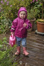 Little girl with rubber boots and rain jacket playing with water and watering can in the rain