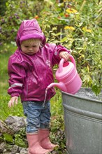 Little girl with rubber boots and rain jacket playing with water and watering can in the rain