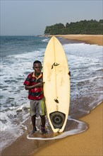 Local boy with his surfboard on a beach in Robertsport