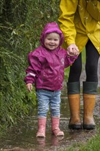 Little girl with rubber boots and rain jacket holding her mother's hand in the rain
