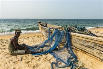 Man fixing his nets in his fishing boats on a beach in Robertsport