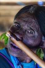 Chin woman with spiderweb tattoo blowing a flute with her nose