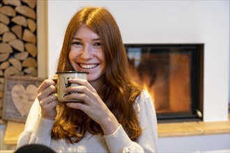 Young woman sitting with a tea cup in front of a fireplace