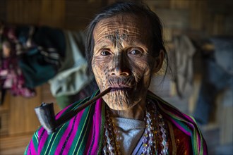 Chin woman with spiderweb tattoo smoking a pipe