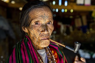 Chin woman with spiderweb tattoo smoking a pipe