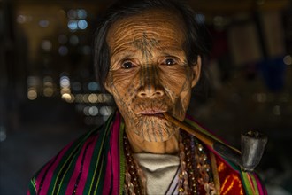 Chin woman with spiderweb tattoo smoking a pipe