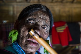 Chin woman with spiderweb tattoo blowing a flute with her nose