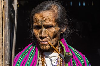 Chin woman with spiderweb tattoo smoking a pipe