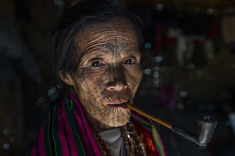 Chin woman with spiderweb tattoo smoking a pipe