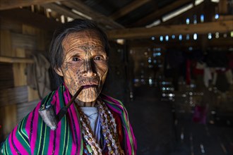 Chin woman with spiderweb tattoo smoking a pipe