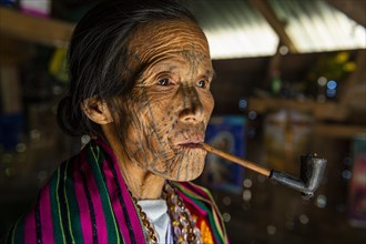 Chin woman with spiderweb tattoo smoking a pipe