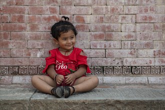 Little girl sitting in front of a house wall