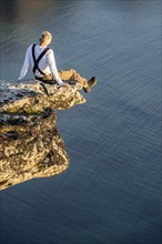 Hiker sitting on rock ledge on precipice above sea
