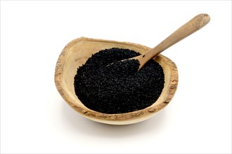 Nigella seeds in a wooden rustic bowl with a wooden spoon against a white background