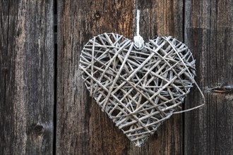 Woven heart hanging on an old wooden facade made of weathered wood