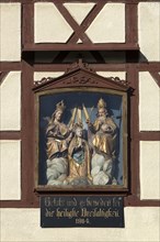 Figures of the Trinity in a glass shrine in the facade of a farmhouse