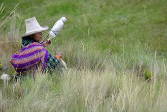 Indigenous woman sitting in the meadow spinning wool