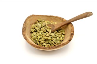 Cardamom pods in a wooden rustic bowl with a wooden spoon against a white background