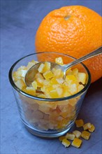 Candied orange peel cubes in glass with spoon