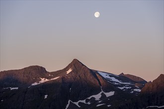 Moon in evening sky over rocky mountains