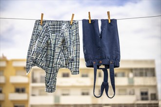 Baby trousers and shirt drying outside with apartment building as a background